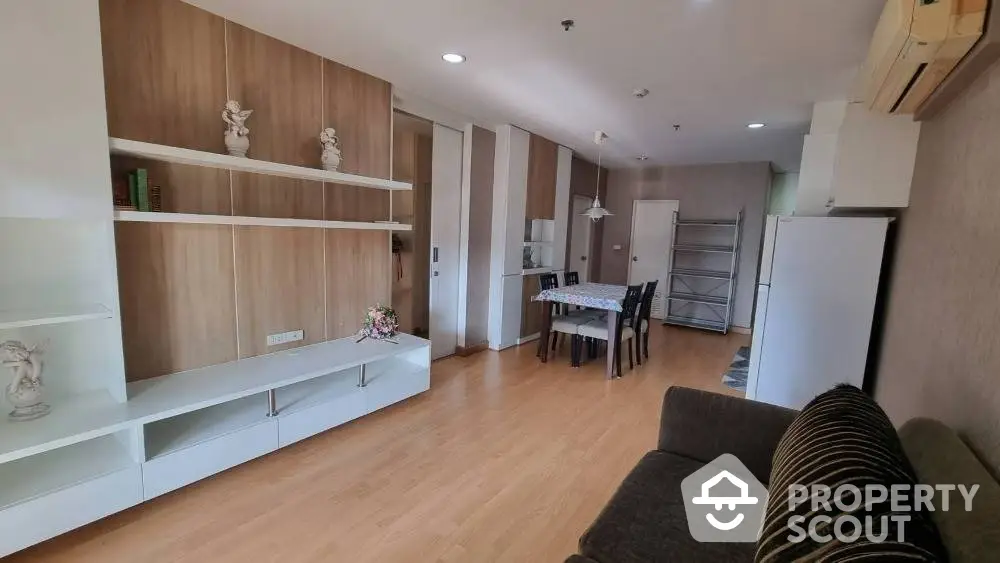 Spacious living room with modern furniture, wooden flooring, and an open layout leading to a well-equipped kitchen area.