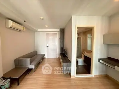 Modern apartment interior with open living room and visible bathroom, featuring sleek furniture and wooden flooring.