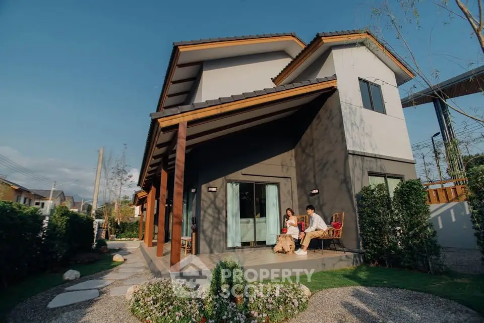 Modern two-story house with lush garden and outdoor seating area.