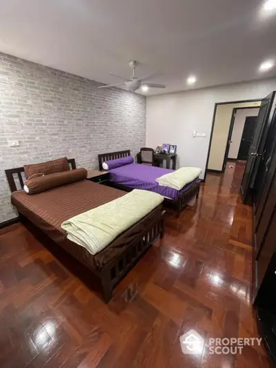 Spacious bedroom with polished wooden flooring, two large beds, and a trendy exposed brick wall, ideal for a modern living experience.