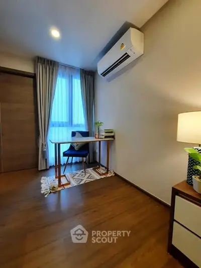 Cozy study room with wooden flooring, air conditioning, and natural light from large window.