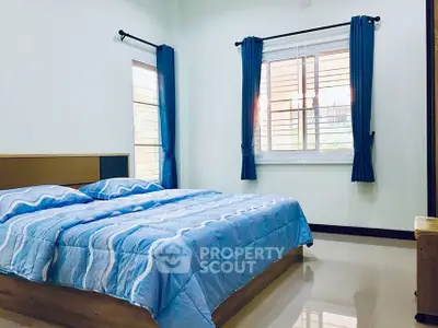 Spacious bedroom with large windows and blue curtains, featuring a cozy bed and polished floors.