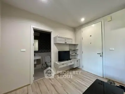 Modern apartment interior with TV and bathroom view, featuring sleek design and light wood flooring.
