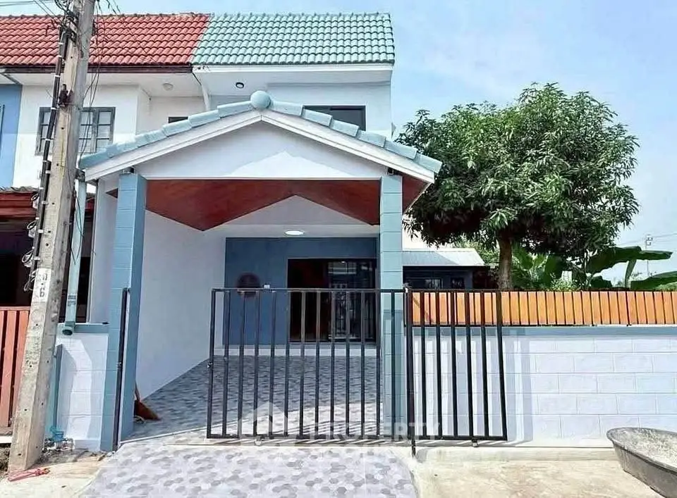 Charming townhouse with gated entrance and tiled patio, featuring a vibrant roof and lush greenery.