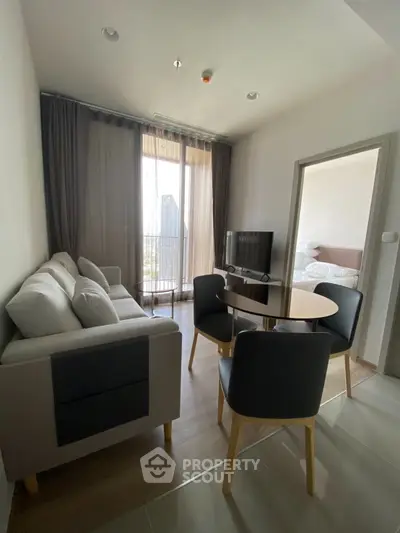 Modern living room with cozy seating and natural light, featuring a view of the balcony.