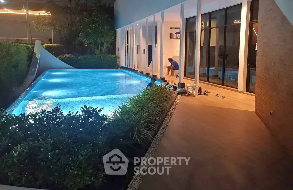 Luxurious modern poolside area with ambient lighting and lush greenery, perfect for relaxation and entertainment.