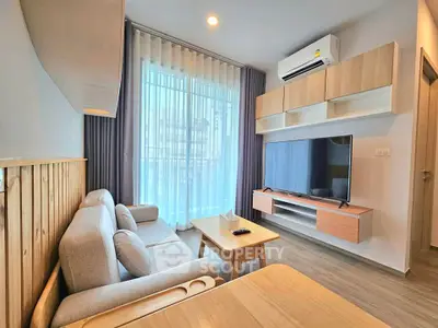 Modern living room with stylish furniture and large TV, featuring natural light and elegant decor.