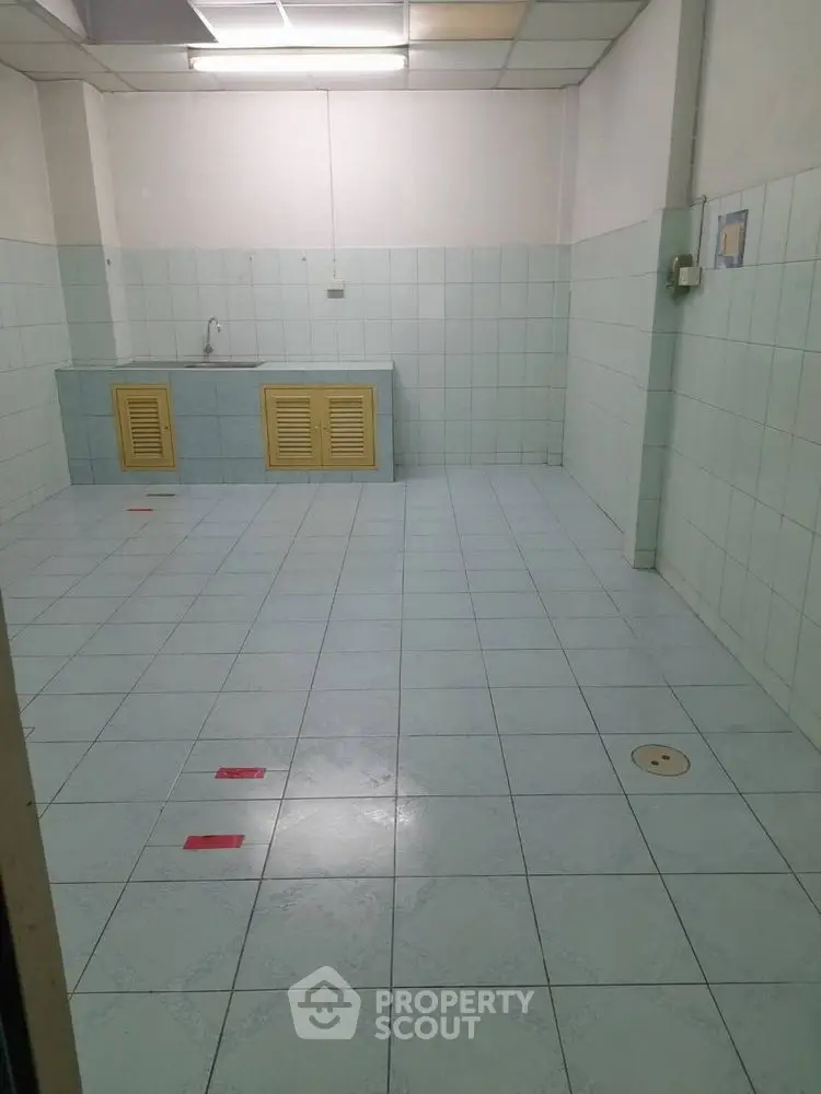 Spacious tiled kitchen area with sink and storage cabinets, ideal for renovation.