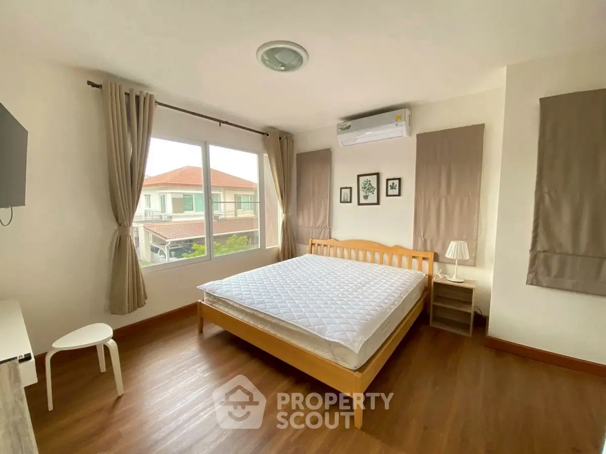 Spacious bedroom with large window and wooden flooring in modern home.