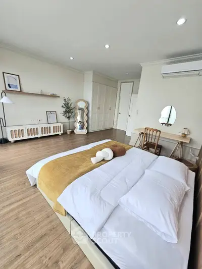 Spacious bedroom with modern decor and wooden flooring, featuring a cozy bed and ample natural light.