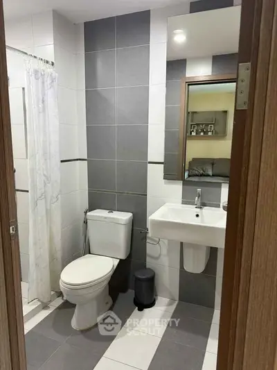 Modern bathroom with sleek gray and white tiles, featuring a toilet, sink, and shower area.