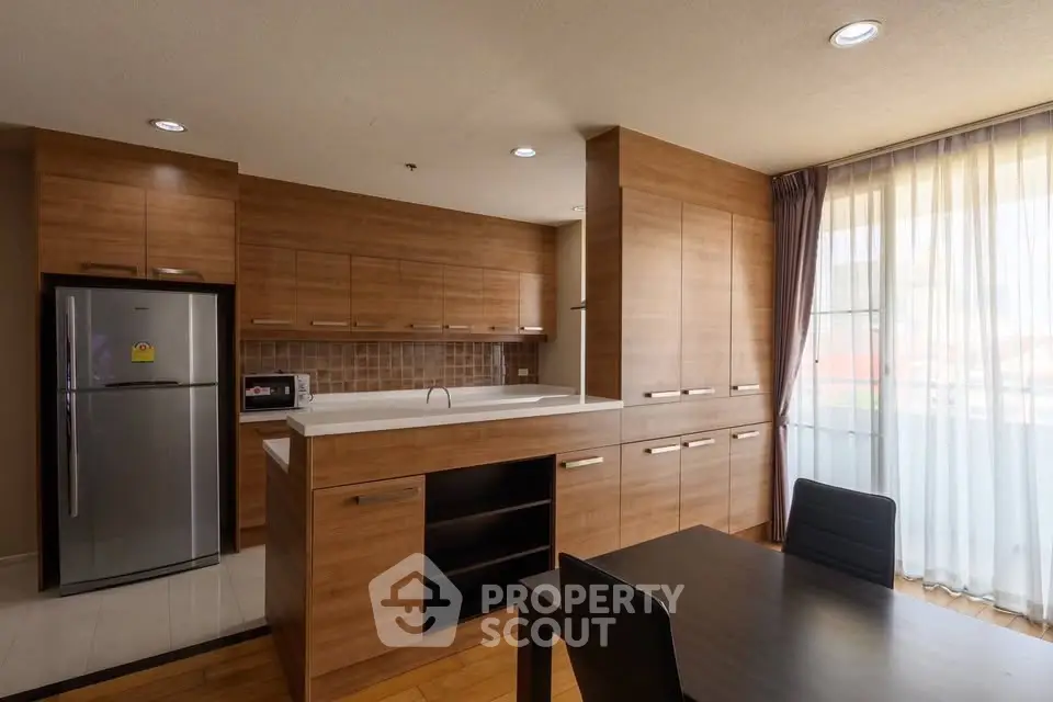 Modern kitchen with wooden cabinetry and dining area in a bright apartment