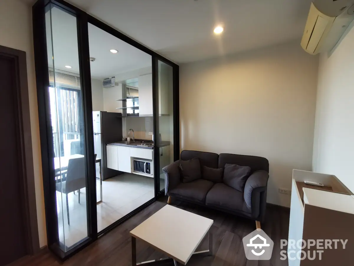 Modern apartment interior featuring sleek furniture, a cozy living area with a dark sofa, and an open layout kitchen with built-in appliances, complemented by ample natural light.