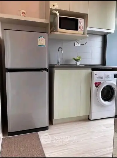 Modern compact kitchen with fridge, microwave, and washing machine in stylish apartment.