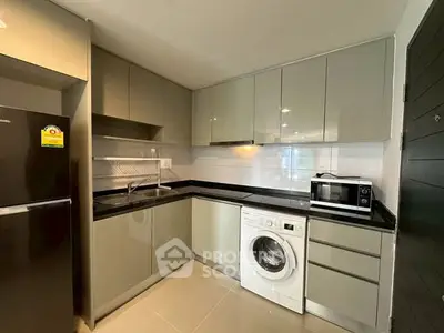 Modern kitchen with sleek cabinetry, washing machine, and microwave in a compact layout.