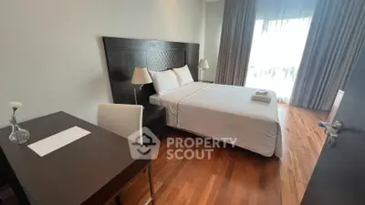 Elegant bedroom with wooden flooring and natural light, featuring a cozy bed and stylish decor.