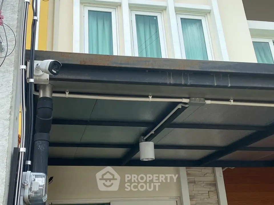 Modern residential building facade with security camera and covered entrance.