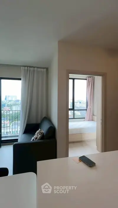 Modern apartment interior with living room and bedroom view, featuring large windows and cityscape.