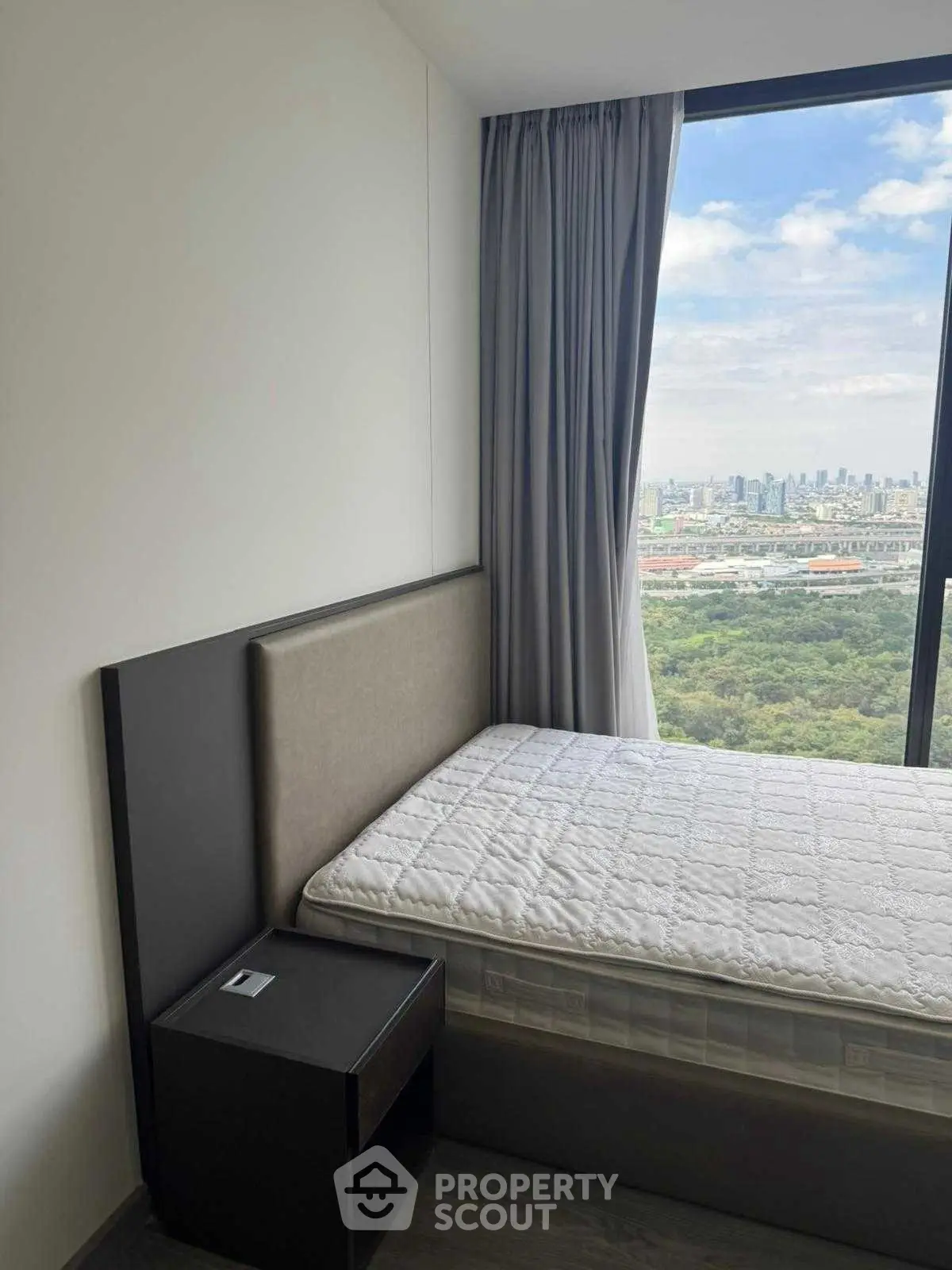 Modern bedroom with stunning city view and large window, featuring a cozy bed and sleek nightstand.