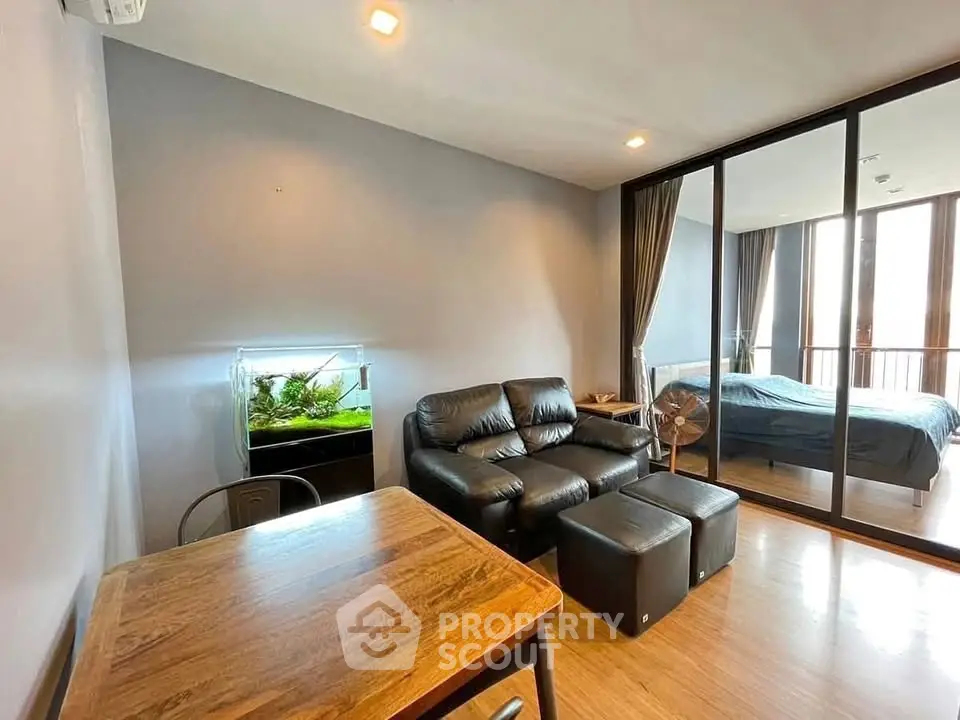 Modern living room with leather sofa, aquarium, and glass partition leading to bedroom.