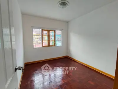 Spacious empty bedroom with wooden flooring and large window for natural light.