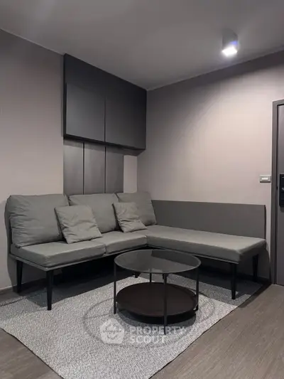 Modern living room with sleek gray sectional sofa and round coffee table on textured rug.