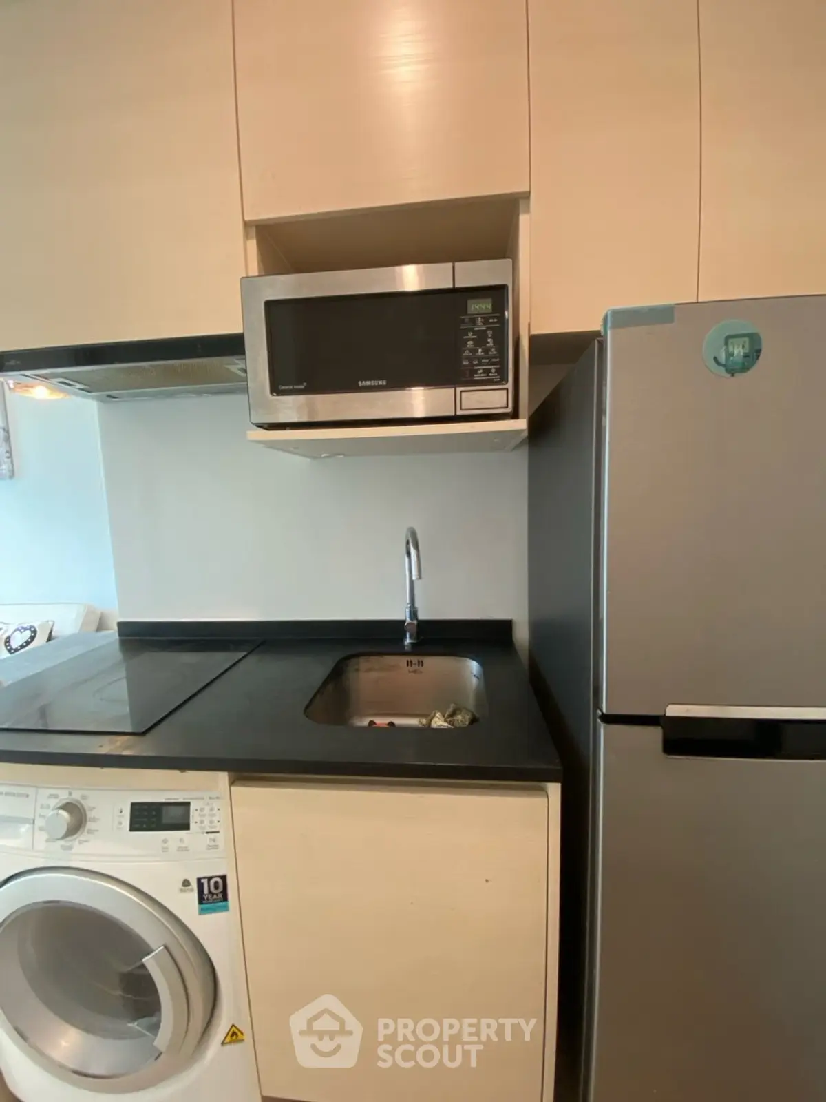 Compact kitchen with modern appliances including washing machine, microwave, and fridge.