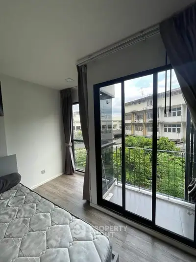 Bright bedroom with large windows and balcony overlooking greenery, perfect for relaxation.