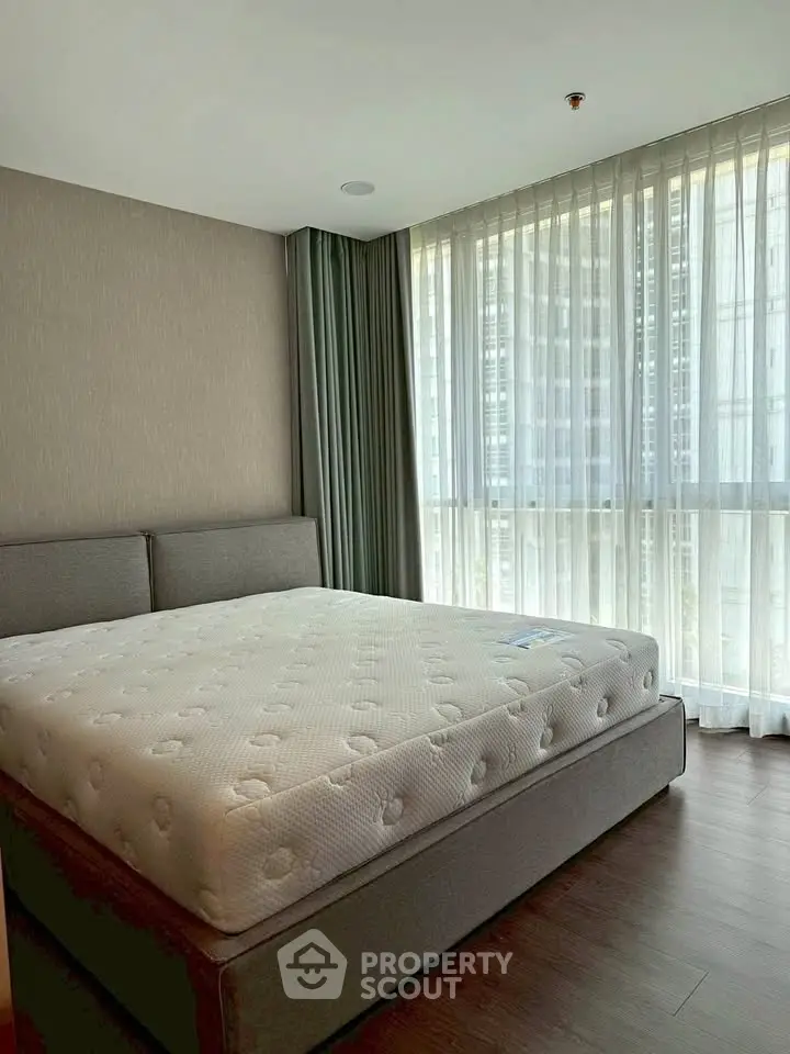 Spacious bedroom with large windows and modern decor in a high-rise apartment.