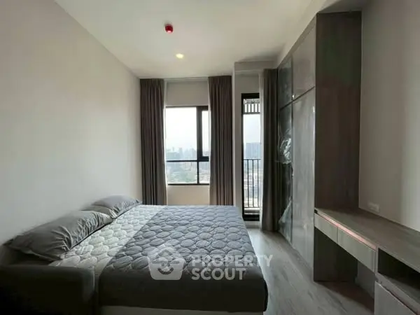 Modern bedroom with large window and city view, featuring sleek furniture and neutral tones.