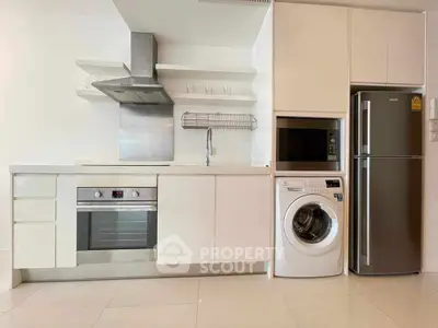 Modern kitchen with sleek appliances including oven, washing machine, and fridge in a bright setting.