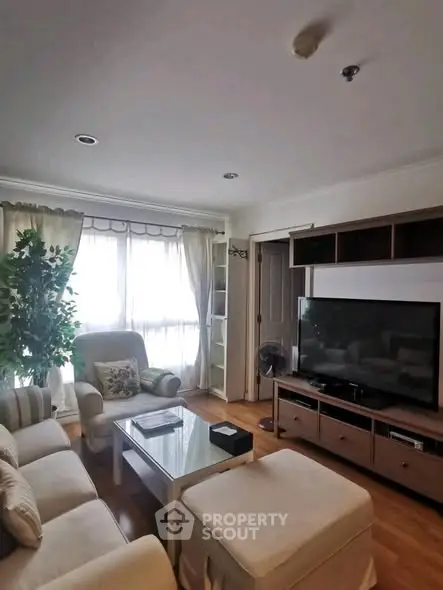 Cozy living room with large TV and natural light, perfect for relaxation.