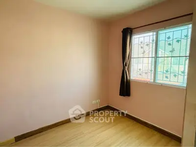 Cozy empty bedroom with wooden flooring and large window for natural light.