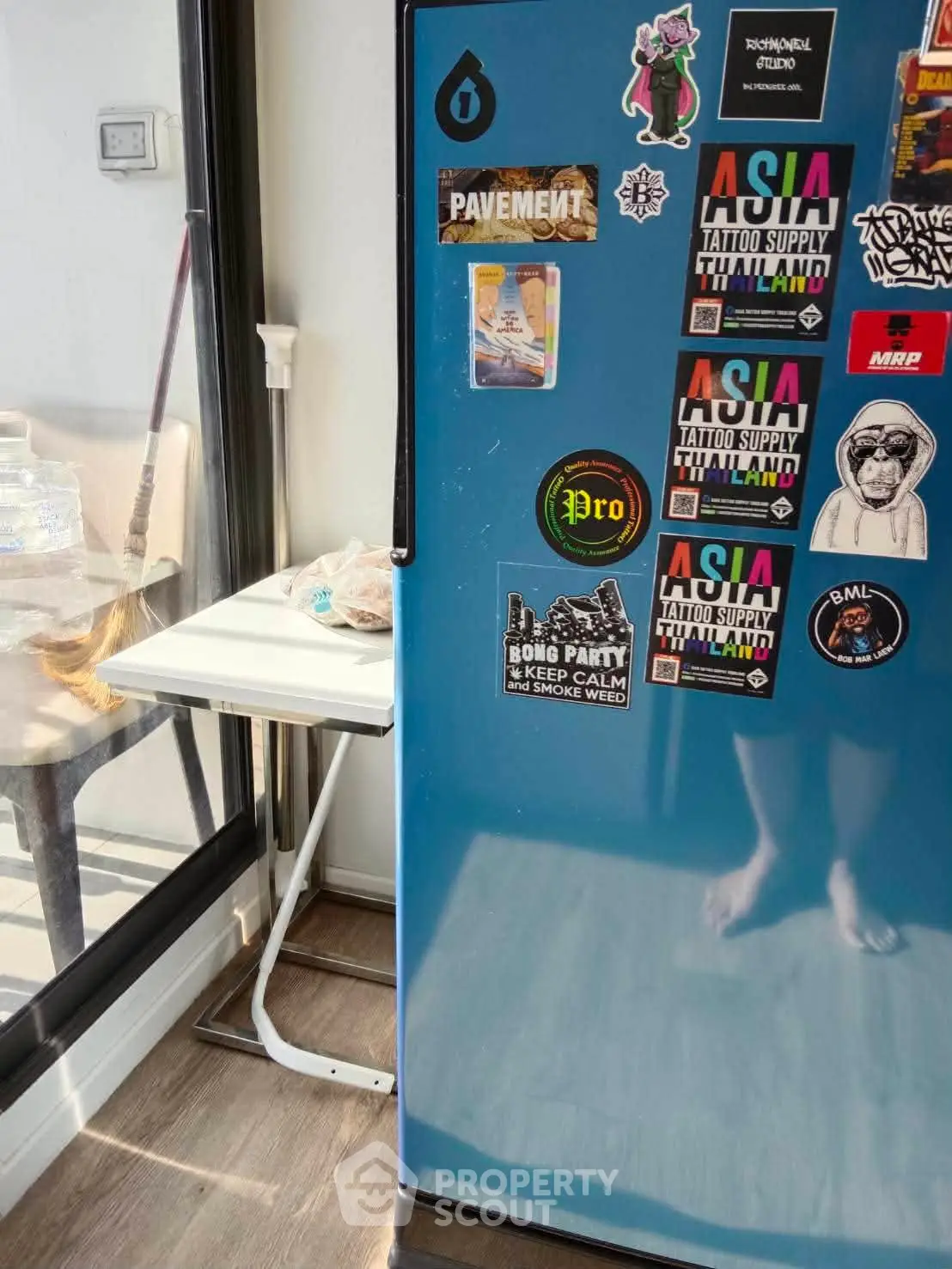 Modern kitchen with blue fridge adorned with colorful stickers, next to a small folding table by the window.