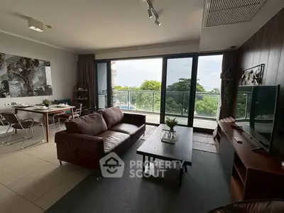 Spacious living room with modern decor and large balcony overlooking lush greenery.