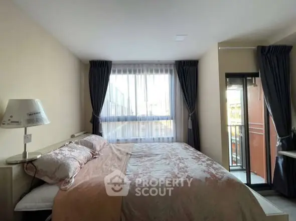 Cozy bedroom with large window and balcony access, featuring elegant curtains and stylish bedding.