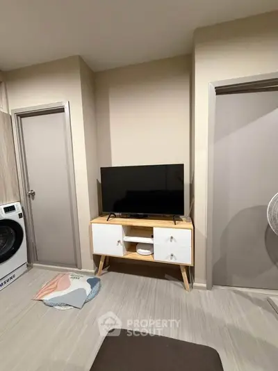 Modern living room with TV stand and washing machine, featuring neutral tones and sleek design.