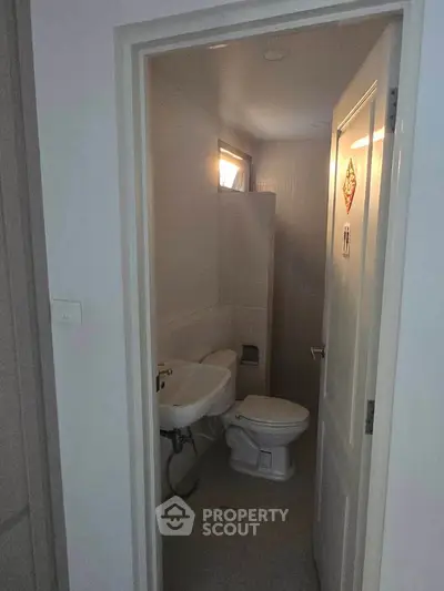 Compact bathroom with white fixtures and natural light from small window.