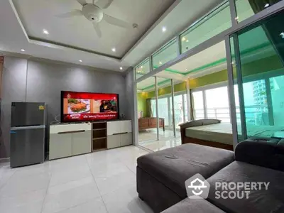 Modern living room with glass wall and balcony view, featuring sleek furniture and ceiling fan.