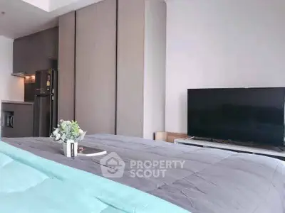 Modern bedroom with sleek design, featuring a cozy bed, flat-screen TV, and stylish kitchen area.