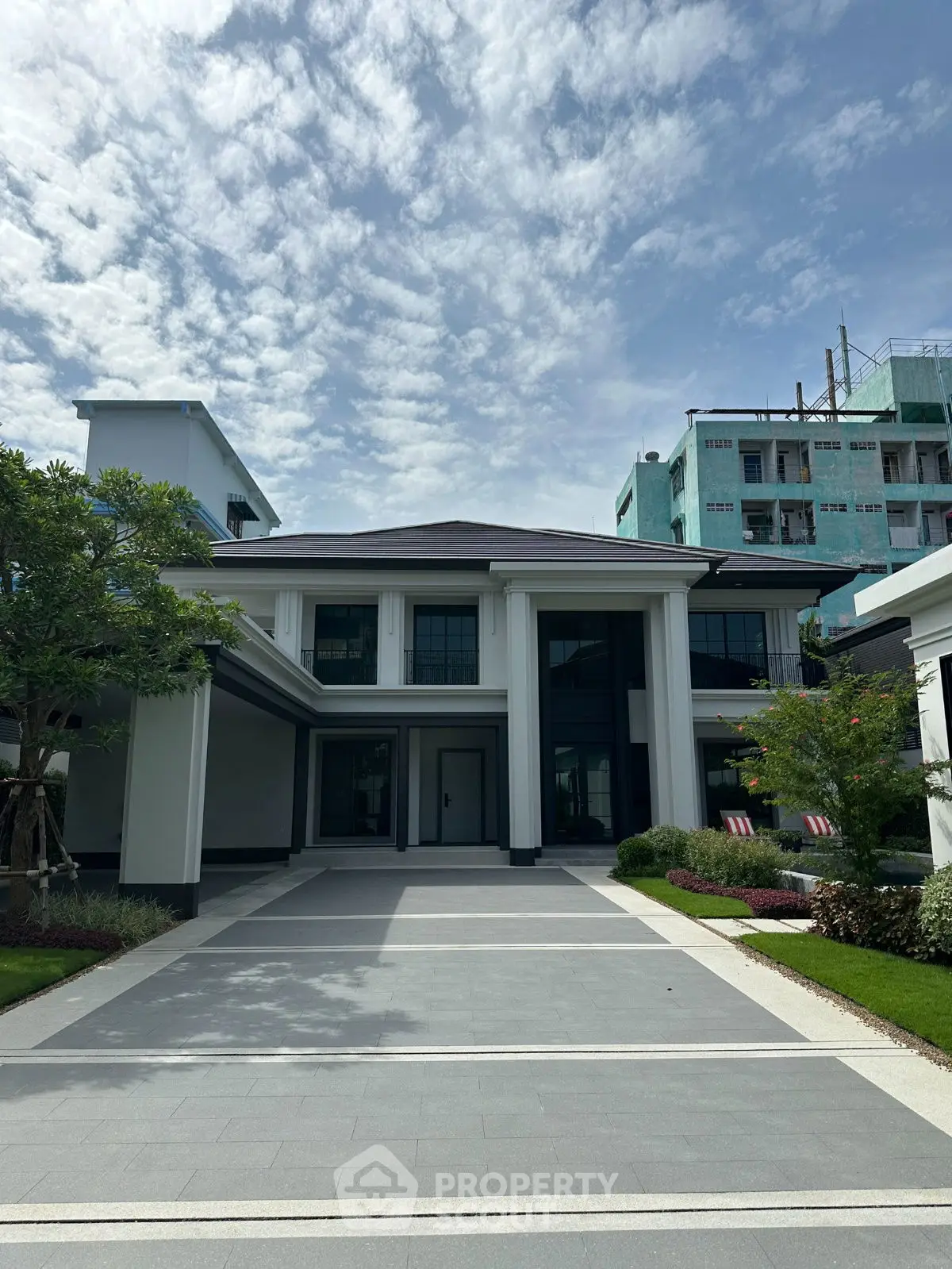 Elegant modern mansion with grand entrance and manicured garden under a clear blue sky.