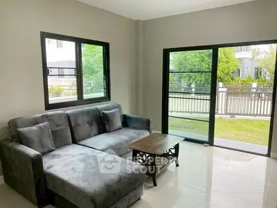 Modern living room with sleek gray sofa and large windows overlooking garden.