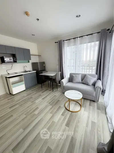 Modern open-plan living room with sleek kitchen and cozy seating area, featuring large windows and stylish decor.