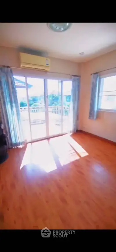 Bright living room with wooden flooring and large windows leading to a balcony.