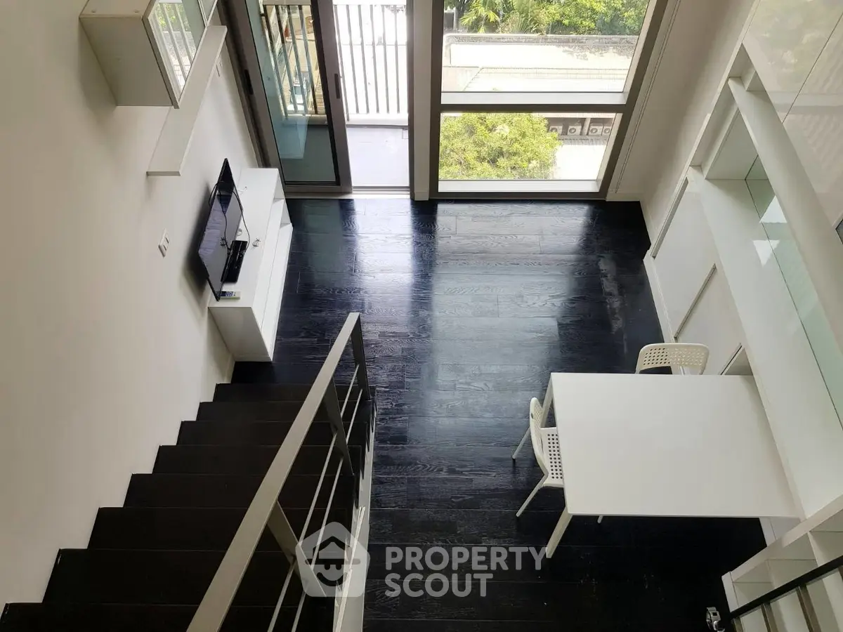Modern loft-style living room with black wooden floors and large windows.