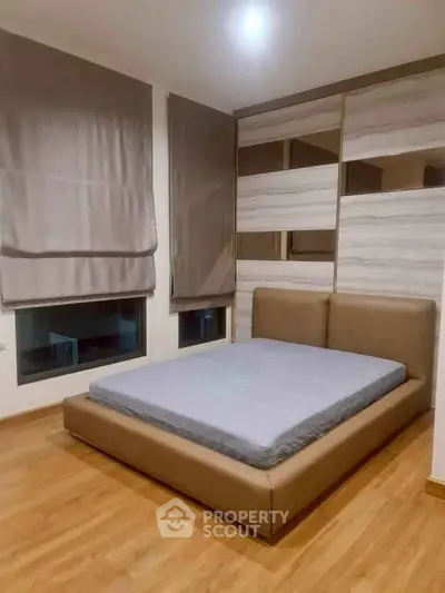 Modern bedroom with stylish bed and wooden flooring, featuring large windows and elegant blinds.