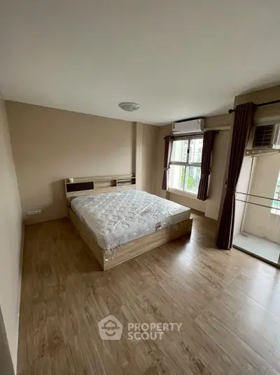 Spacious bedroom with wooden flooring and large windows in modern apartment.