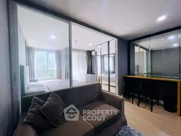 Modern apartment interior with cozy living room and bedroom separated by glass partition.