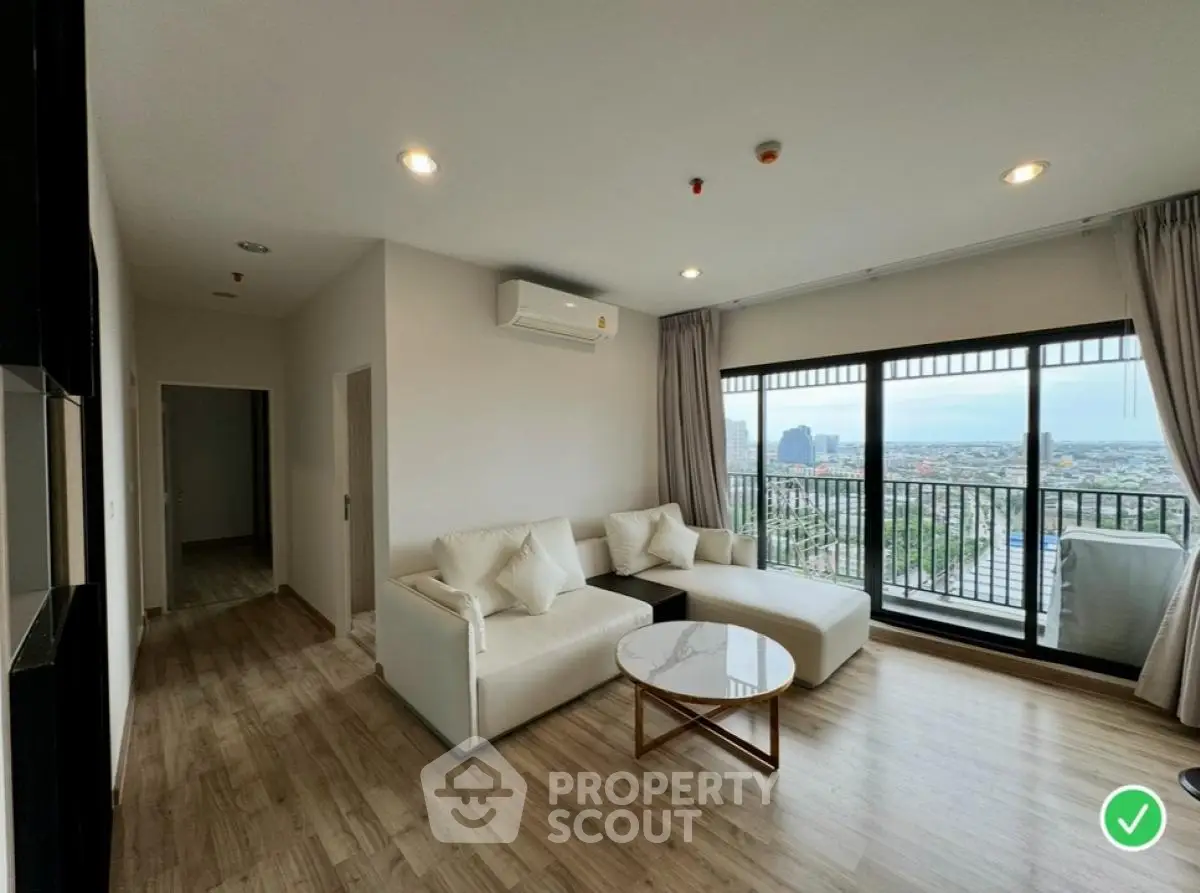 Modern living room with large windows and city view, featuring stylish furniture and wooden flooring.