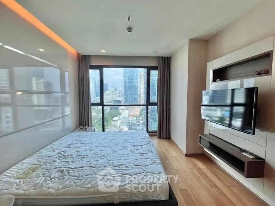 Modern bedroom with city view, large window, and wall-mounted TV in a high-rise apartment.